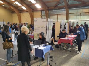 Photo d'un forum avec plusieurs stand et des gens qui discutent autour de ces stands. Le forum est dans un gymnase. 