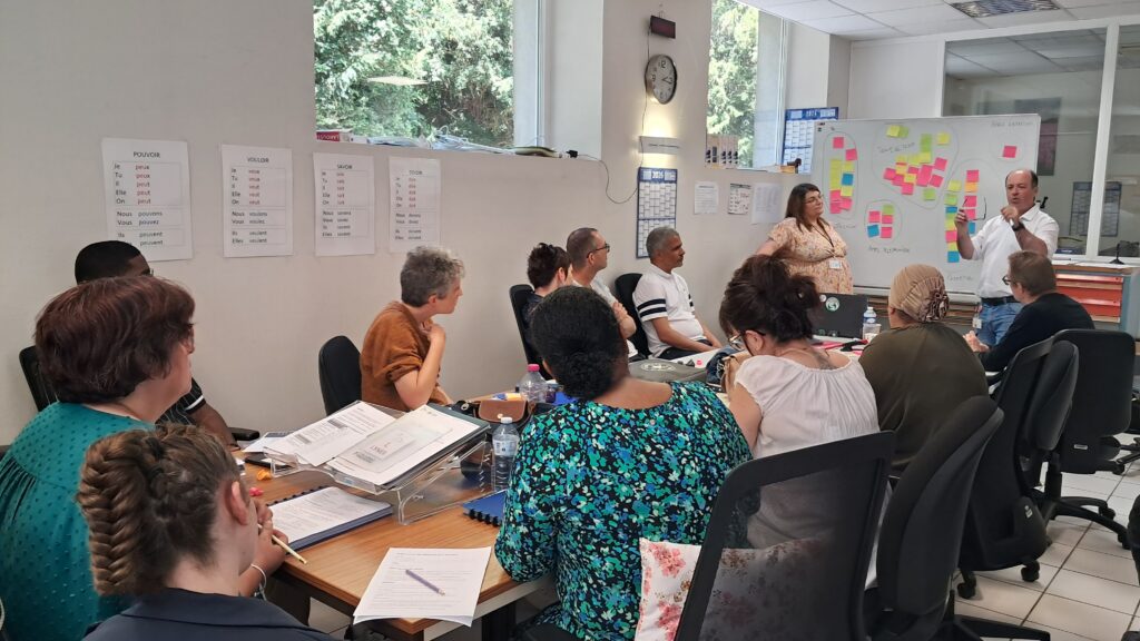 Réunion de travail avec plusieurs participants autour d’une table, pendant une présentation animée devant un tableau rempli de notes colorées - rencontre avec le service RH d'APRR