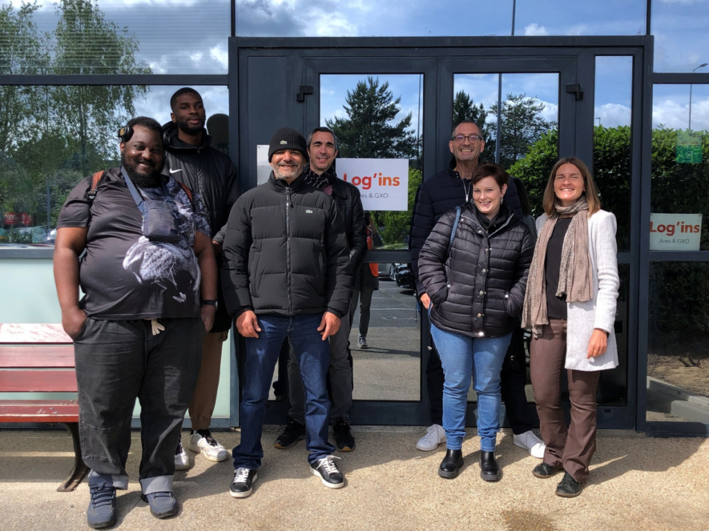 Un groupe de personnes pose souriant devant l’entrée d’un bâtiment lors d’une visite ou d’une rencontre professionnelle avec Log’ins - Découverte des métiers de la logistique