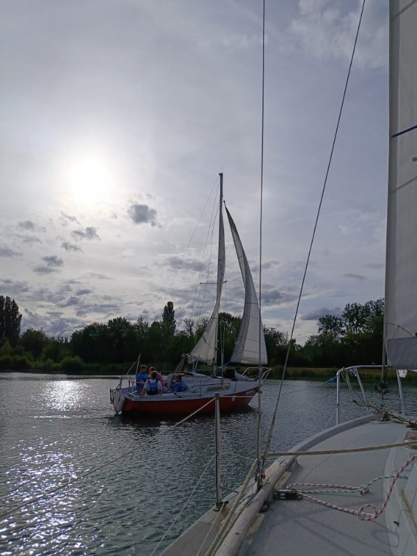 Un voilier navigue sur un plan d’eau calme, observé depuis un second bateau sous un ciel nuageux - Cap sur la confiance : initiation à la voile