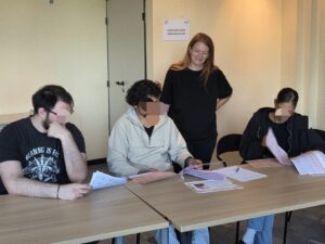 parcours santé remobilisation - Trois participants sont assis autour d'une table et consultent des documents sous le regard souriant d'une animatrice debout derrière eux. L'action se déroule dans une salle de formation.