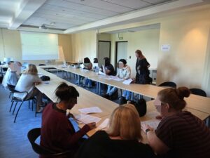 Parcours santé remobilisation - Un groupe de participants est assis autour de tables disposées en U dans une salle de formation, consultant des documents sous la conduite d'une animatrice debout. Un écran de projection est visible au fond de la pièce